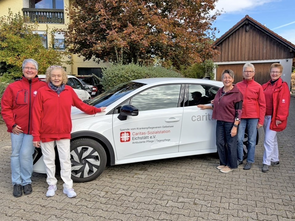 Fünf Leute stehen vor Caritas-Auto